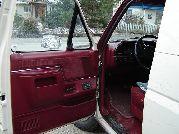 Interior of a white truck with red door panels and seats, viewed from the driver's side