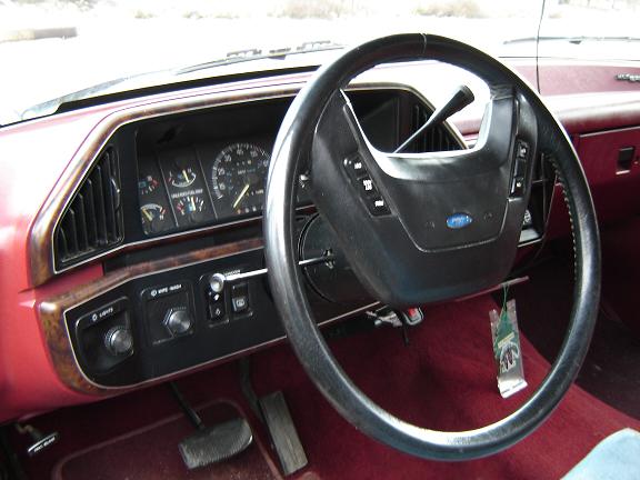Interior shot of a car's dashboard with a steering wheel, gauges, and red carpet