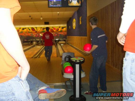Bowling alley with people bowling, bowling balls, and pins