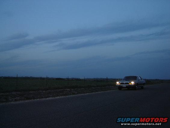 1988 Ford Crown Victoria LTD driving on a road at dusk, headlights on