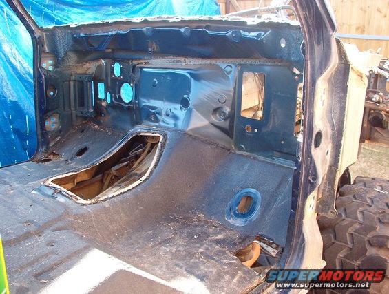 Disassembled vehicle interior showing exposed metal floor and firewall, with blue tarp in background