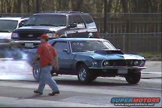 Blue 1969 Ford Mustang drag car with hood scoop, emitting smoke from rear tire