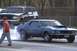 1969 Ford Mustang - A blue 1969 Ford Mustang performs a burnout on a drag strip, with an SUV in the background.