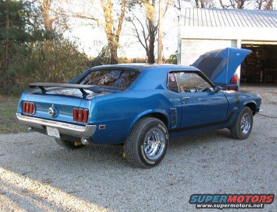 Blue 1969 Ford Mustang with hood open, parked on gravel near a garage