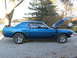 1969 Ford Mustang - Side view of a blue 1969 Ford Mustang coupe, black racing stripes and a spoiler, parked outdoors with its hood up.