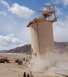 1979 Ford Bronco - Dust billows from the base of a large industrial silo, with several vehicles and construction equipment visible in the arid landscape.