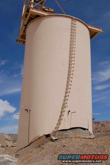 Damaged industrial silo with ladder against blue sky