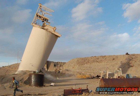 Person running from tilted silo in desert landscape