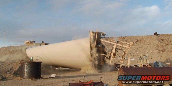Large cylindrical object falling, kicking up dust, with wooden supports