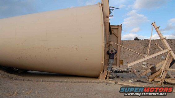 Fallen tan silo with a person on a ladder next to it. Debris and construction materials are scattered around