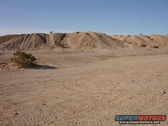 Desert landscape with tire tracks on sandy ground and a distant hill