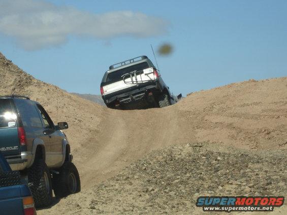 Two SUVs off-roading on a steep dirt incline under a blue sky
