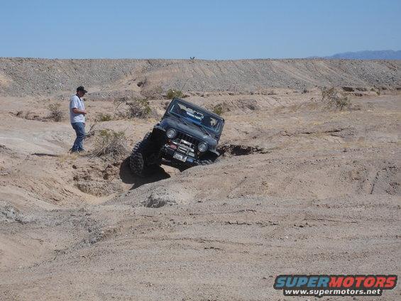 Dark Jeep Wrangler climbing a dirt hill in a desert landscape