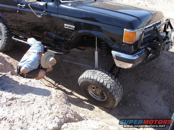 Black Ford Bronco with lifted suspension and off-road tires, a person crouches underneath