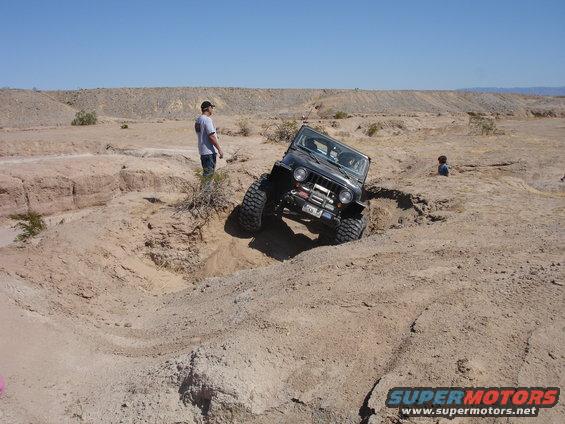 Black Jeep Wrangler TJ with large tires going down a steep dirt embankment, person watching