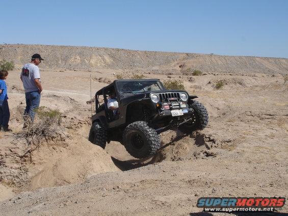 Black Jeep Wrangler with large tires navigating a dirt obstacle, front view