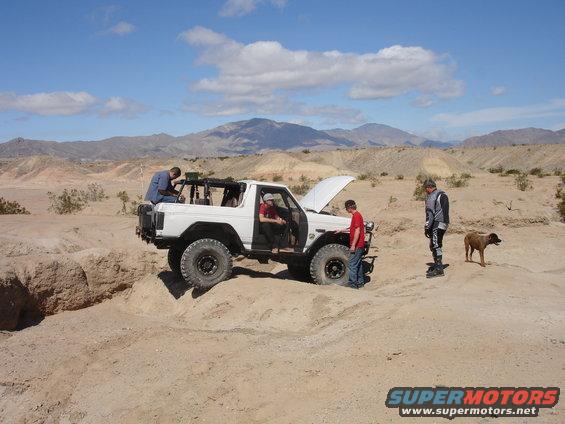 1996 Ford Bronco with hood open, stuck in desert dirt, people attending to it