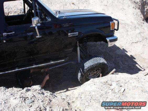 Black Ford Bronco with lifted suspension stuck in dirt, person underneath working on it