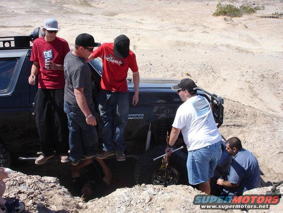 People trying to get a 1996 Ford Bronco unstuck from a hole in the desert
