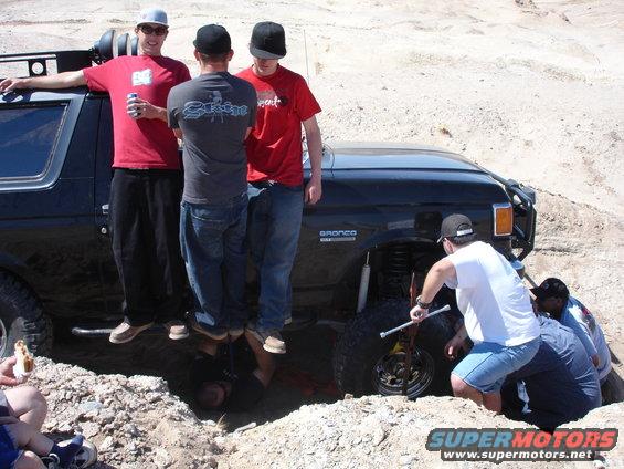 1996 Ford Bronco stuck in dirt, people working on wheel
