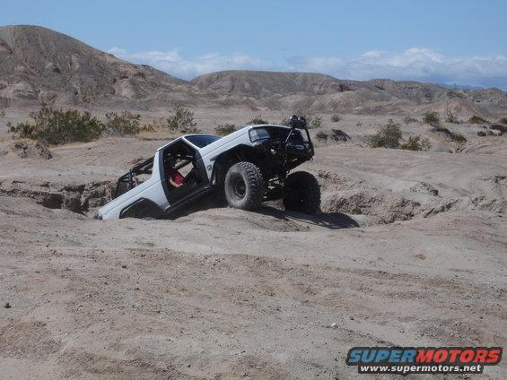 1996 Ford Bronco off-roading, one front wheel in a ditch, roll cage visible