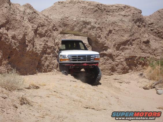1996 Ford Bronco driving through a natural rock arch in a desert landscape