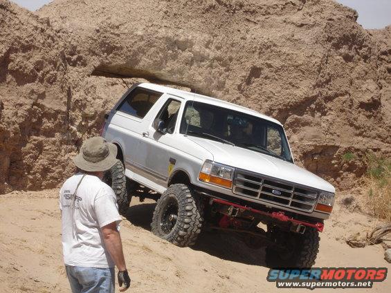 White 1996 Ford Bronco climbing a sandy hill with a person watching