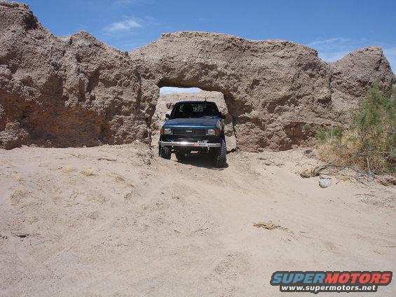 Dark blue SUV with a chrome bumper driving through a natural rock archway in a desert landscape