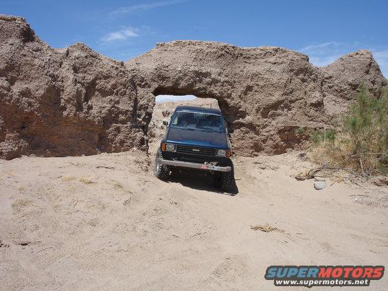 Blue SUV driving through a rock archway in a desert landscape