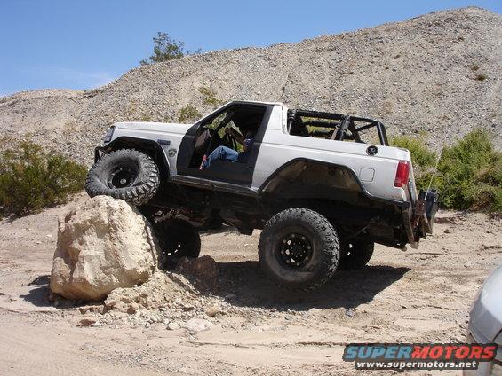 White SUV with large tires climbing over a rock on a dirt trail