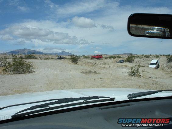 Desert scene with several SUVs and trucks off-roading, view from inside a vehicle