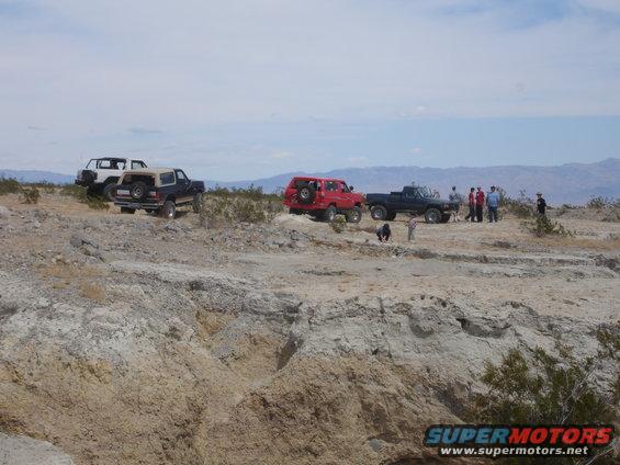 Dark blue Ford Bronco with a tan top and spare tire on the back, parked on a dirt hill