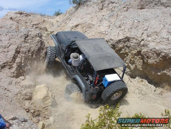 Jeep Wrangler climbing a rocky, dusty trail with a driver wearing a hat