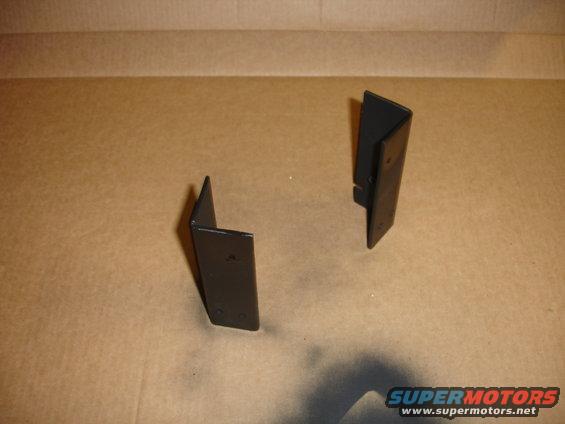 Two black metal brackets with screw holes, resting on a cardboard surface