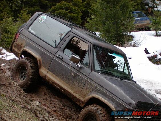 Mud-covered 1987 Ford Bronco II on a muddy incline with snow in the background
