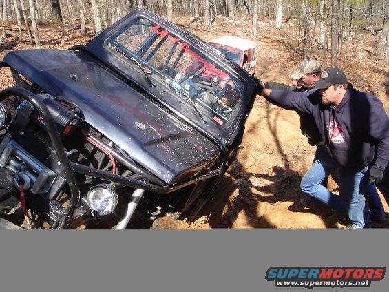 Black off-road vehicle stuck in mud with people trying to push it
