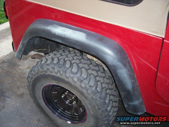 Jeep Wrangler rear fender with black fender flare and off-road tire. Red body panel has scratches