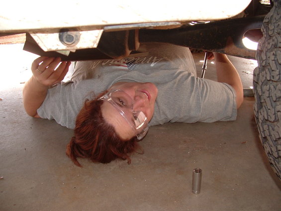 Person working under a vehicle, focusing on the undercarriage and tire
