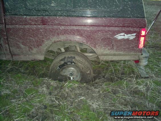 Muddy red truck stuck in the ground, rear wheel sunk deep