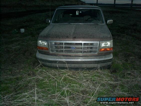 Front view of a dusty brown 1994 Ford Bronco parked in tall grass