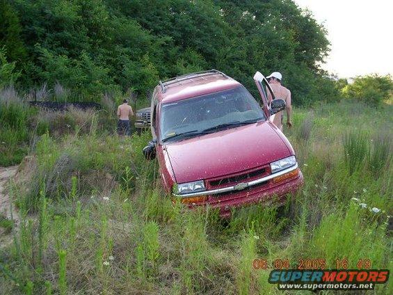 Red Chevrolet SUV with its front end angled into tall grass, driver's door open, and a man exiting