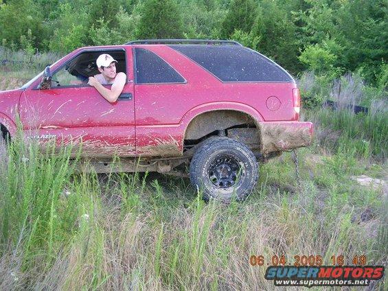 Red SUV side view, covered in mud, with a person leaning out the window