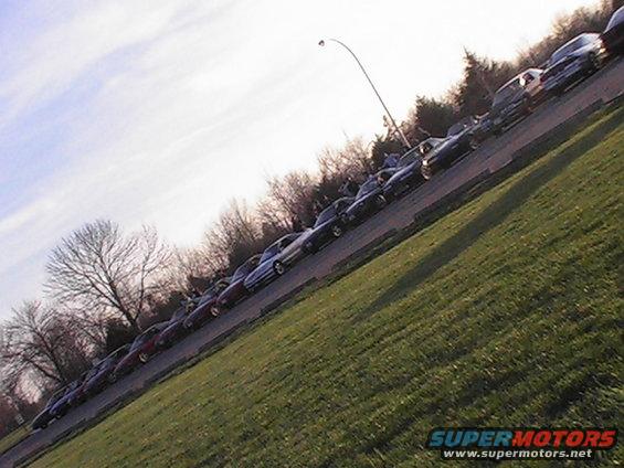 Line of cars parked on a street, viewed from a high angle. Cars are mostly dark colored