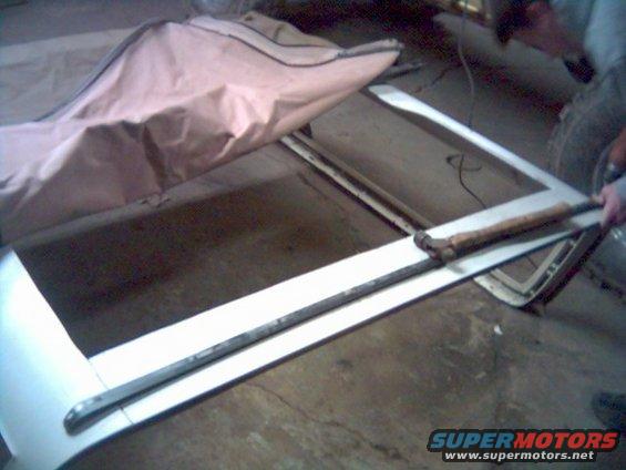 White soft top frame with a tan cover draped over it. A tool rests on the frame