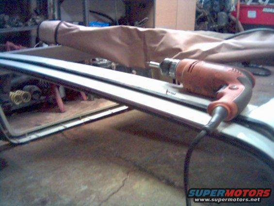 Orange drill resting on a car's roof frame with a tan cover in the background