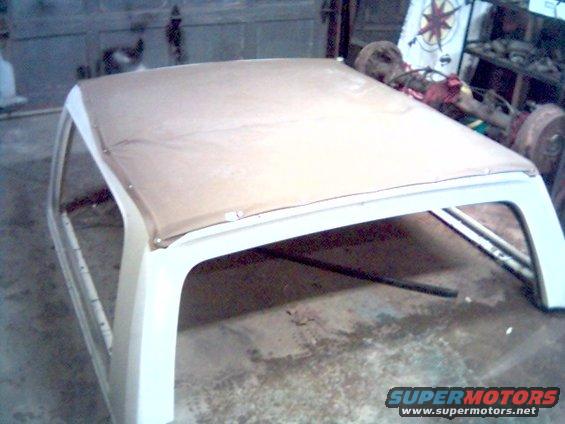 Tan soft top frame on a white vehicle body, viewed from above