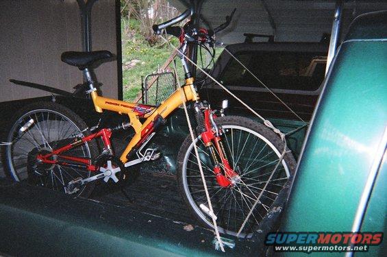 Yellow and red mountain bike secured in the bed of a green pickup truck