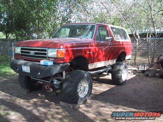 Red lifted 1990 Ford Bronco with large tires and custom bumper