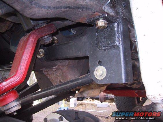 Undercarriage of a vehicle with red and black metal components, bolts, and suspension parts visible