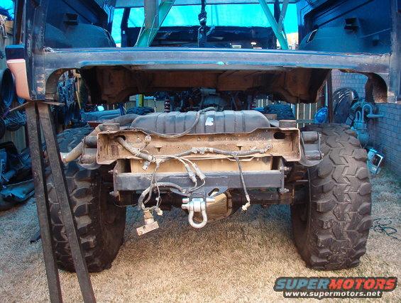 Rear view of a vehicle frame with large off-road tires, fuel tank, and suspension components visible